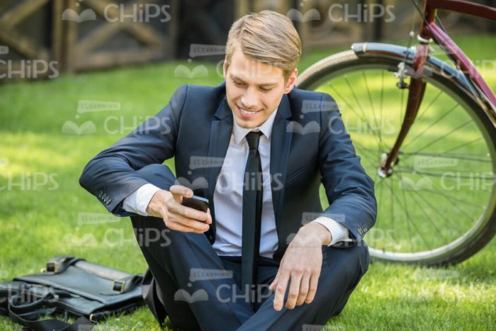 Young Businessman Sitting On Grass And Using His Phone Stock Photo