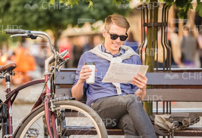 Young Man With Bike Resting Outdoor: Sitting On Bench, Drinking Coffee and Using Tablet