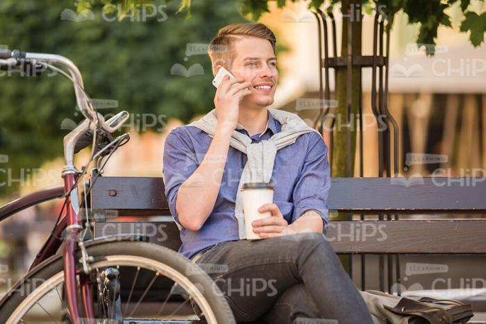Nice Young Man Sits On Bench And Talks On Mobile Phone Stock Photo