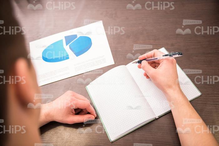 Man's Hand Holding Pen And Making Notes In Notebook Stock Photo