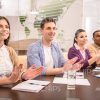 Happy Students Sitting Behind The Table And Applauding Stock Photo