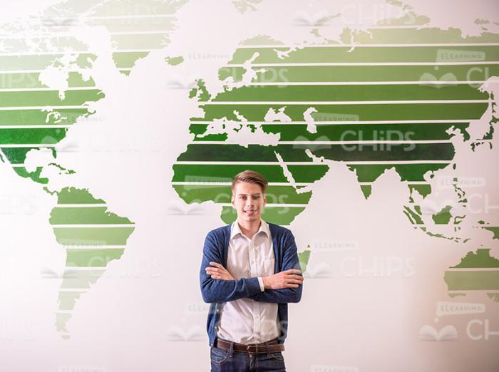 Self-Confident Young Man Crosses Arms And Stands In Front Of World Map Stock Photo