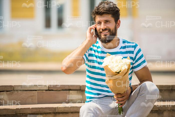 Bearded Young Guy With Bouquet Talks On Mobile Phone Stock Photo