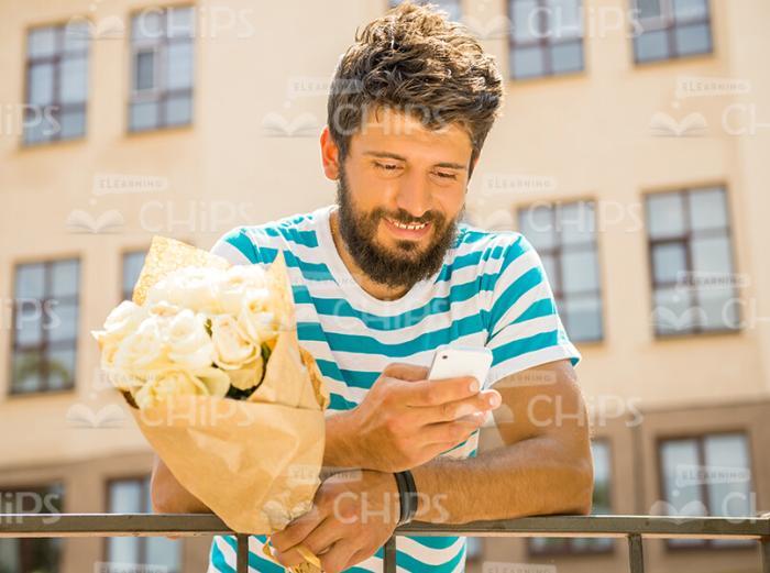 Bearded Young Man With Bouquet And Mobile Phone In Stripped T-shirt Leaning On Railing Stock Photo