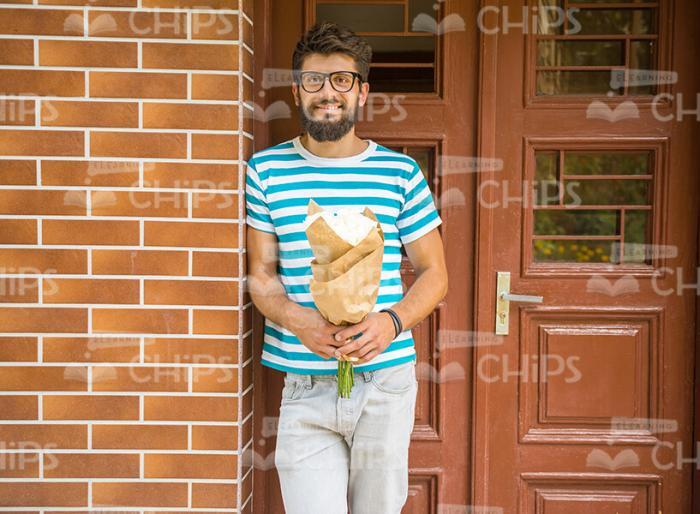 Young Man Standing Next To Door And Holding Bouquet Stock Photo
