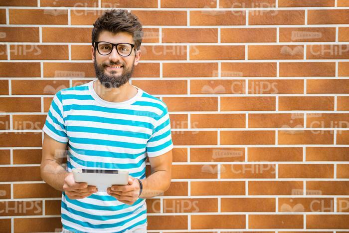 Young Bearded Man With Tablet Standing In Front of Brick Wall Stock Photo