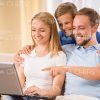 Family Using Laptop And Young Father Pointing On Its Display Stock Photo