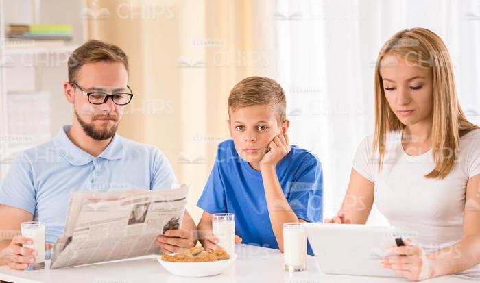 Upset Family Having Breakfast Time While Reading Newspapers And Using Tablet Stock Photo