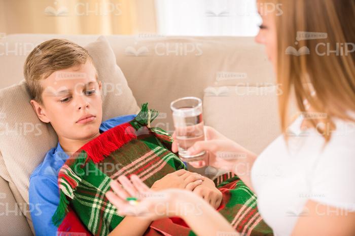 Mother Holds Glass Of Water And Gives Pills To Her Son Stock Photo
