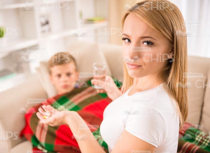 Young Woman Giving Her Son Medicines And Water Stock Photo
