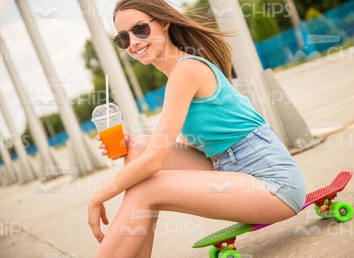 Smiling Girl Sits On Skateboard And Holds Cup With Juice Stock Photo