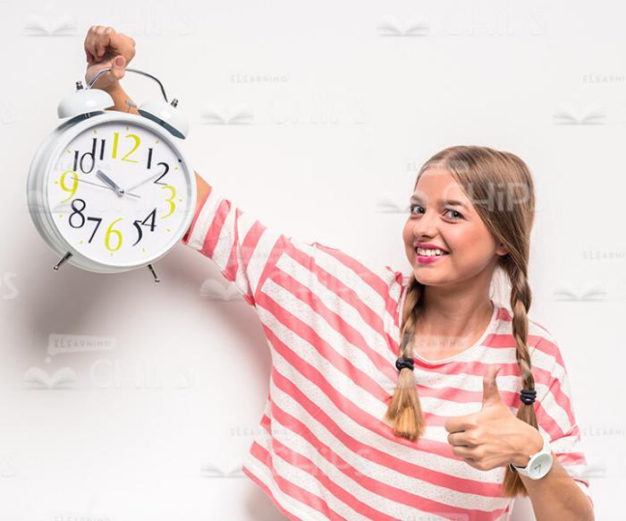 Young Girl Holding Clock And Showing Thumb Up Gesture Stock Photo