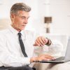 Mid Aged Businessman With Laptop Looking On Clock Stock Photo