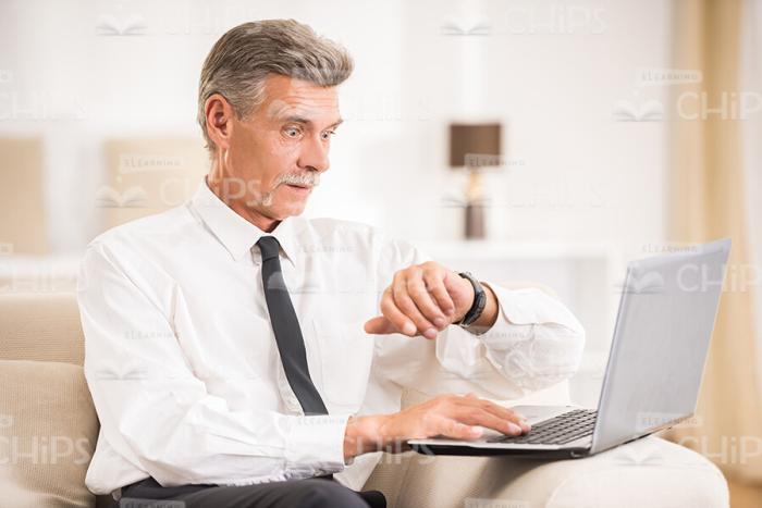 Mid Aged Businessman With Laptop Looking On Clock Stock Photo