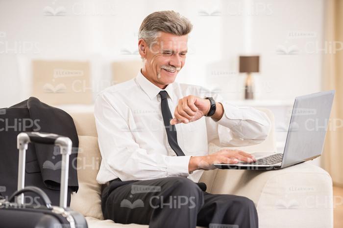 Smiling Man With Laptop Looks At Clocks Stock Photo