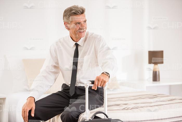 Aged Businessman With Suitcase Sitting In Hotel Room Stock Photo