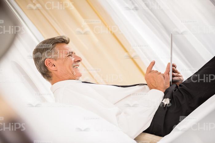 Aged Businessman Resting On Bed And Using Tablet Profile View Stock Photo