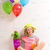 Nice Girl Sits On Floor While Holds Skateboard With Balloons And Orange Juice Stock Photo