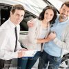 Happy Couple And Car Salesman Standing Next To Vehicle Stock Photo