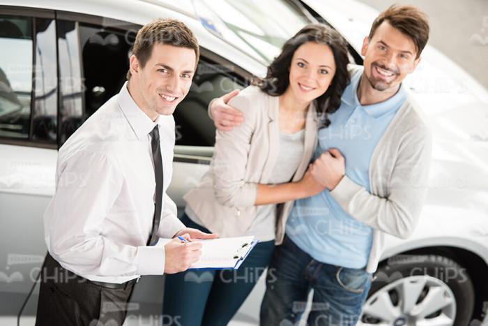 Happy Couple And Car Salesman Standing Next To Vehicle Stock Photo