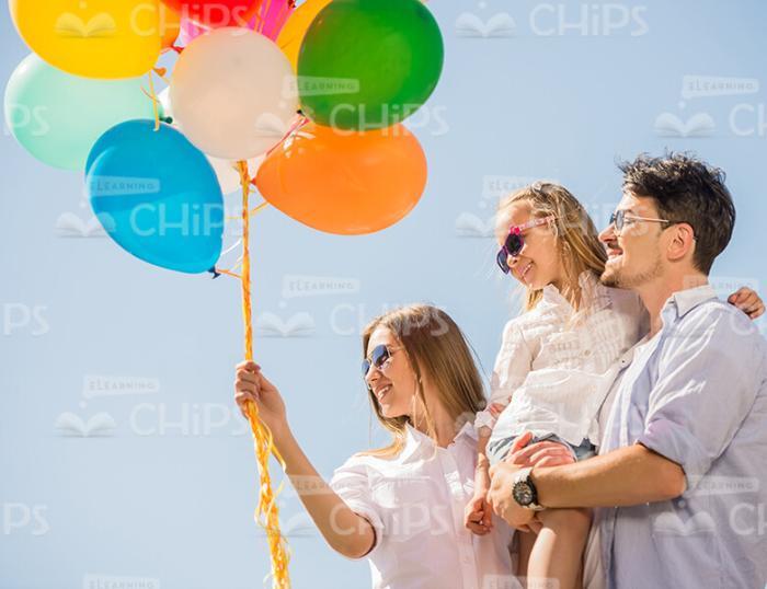 Young Woman Holding Balloons While Walking With Husband And Daughter Stock Photo