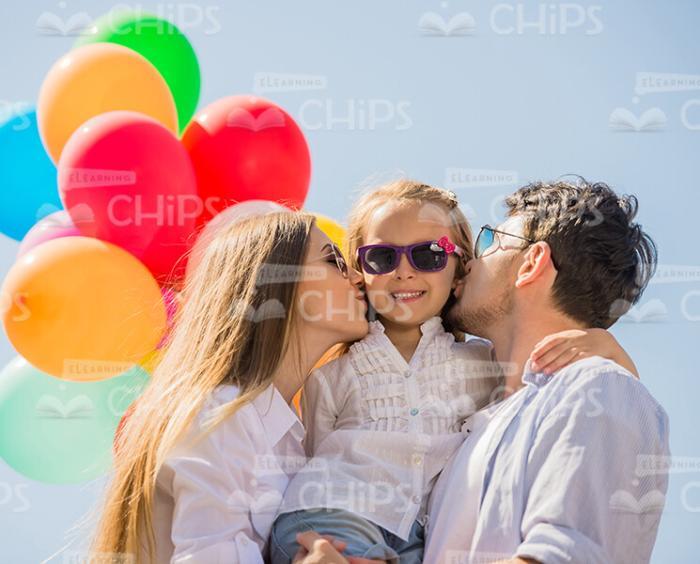 Both Parents Kissing Daughter In Cheeks Stock Photo