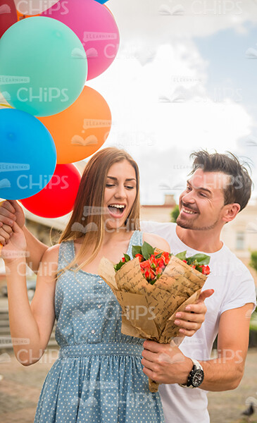 Smiling Young Guy Presenting Bouquet To Woman With Balloons Stock Photo