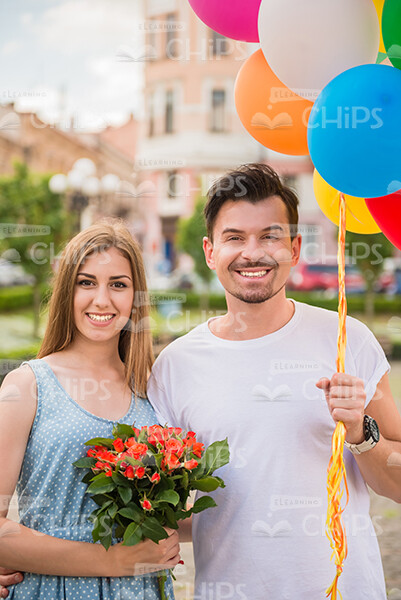 Young Man With Colorful Ballons And Woman With Bouquet Of Flowers Stock Photo