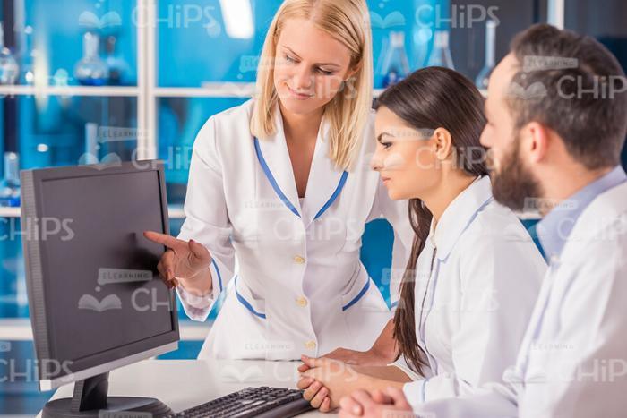 Blonde Female Scientist Pointing At Monitor While Showing Smth. To Colleagues Stock Photo