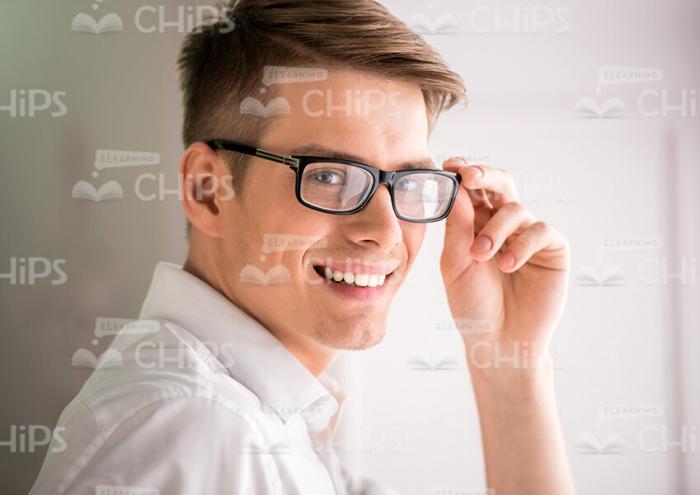 Young Businessman Smiles And Touches To Glasses Stock Photo