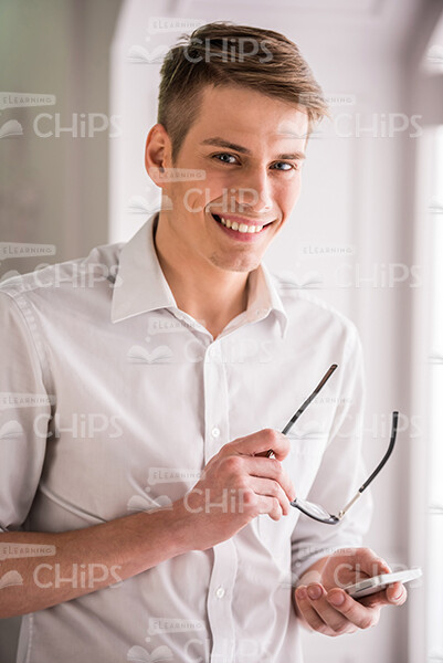 Young Businessman Holds Eyeglasses and Smartphone Stock Photo Young Businessman Holds Eyeglasses and Smartphone Stock Photo