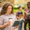 Curly Young Woman Reading Book And Holding Coffee Cup Stock Photo