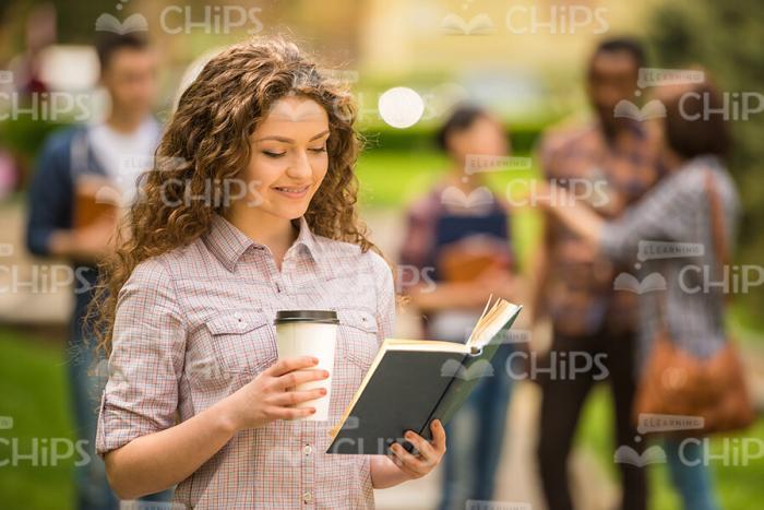 Curly Young Woman Reading Book And Holding Coffee Cup Stock Photo