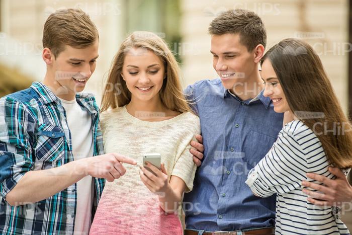 Four Young Friends Look At Mobile Phone's Screen Stock Photo