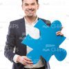Young Businessman Smiles And Holds Large Piece Of Puzzle Stock Photo
