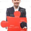 Smiling Guy Holding Big Piece Of Puzzle With Both Hands Stock Photo