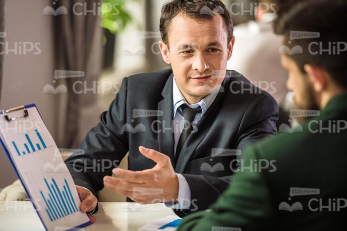 Businessman With Graphs Explaining Something To Colleague Stock Photo