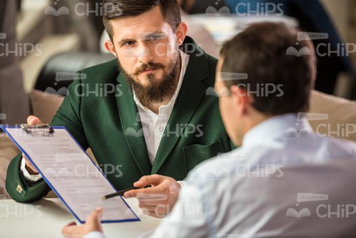 Bearded Business Man Pointing With Pen At Clipboard Stock Photo