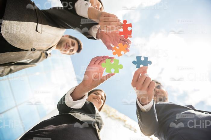 Four People Connecting Puzzle Pieces Stock Photo