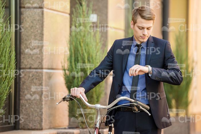 Young Man With Bicycle Looking On Clocks Stock Photo