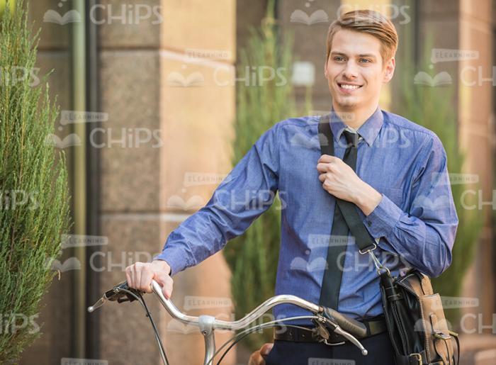 Smiling Business Man With Backpack Holding Bike Stock Photo