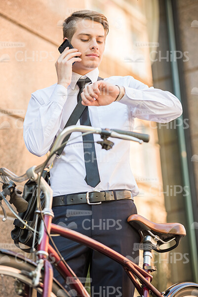 Serious Young Man Talking On Phone And Looking At Watch Stock Photo