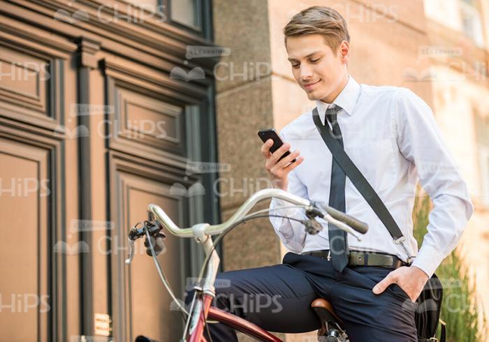 Young Male Character Sitting On Bike And Using His Mobile Phone Stock Photo