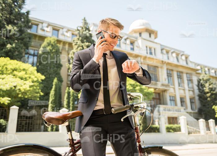 Young Businessman Looking On Watch While Holding Phone Conversation Stock Photo